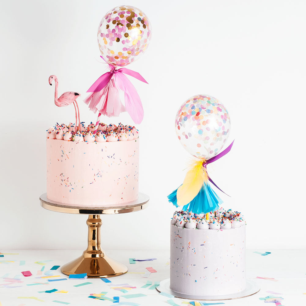 Two buttercream cakes with piping, sprinkles, and balloon cake toppers