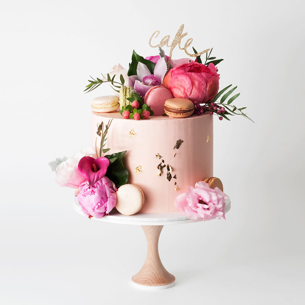 Pink buttercream cake with flowers, macarons, and gold leaf