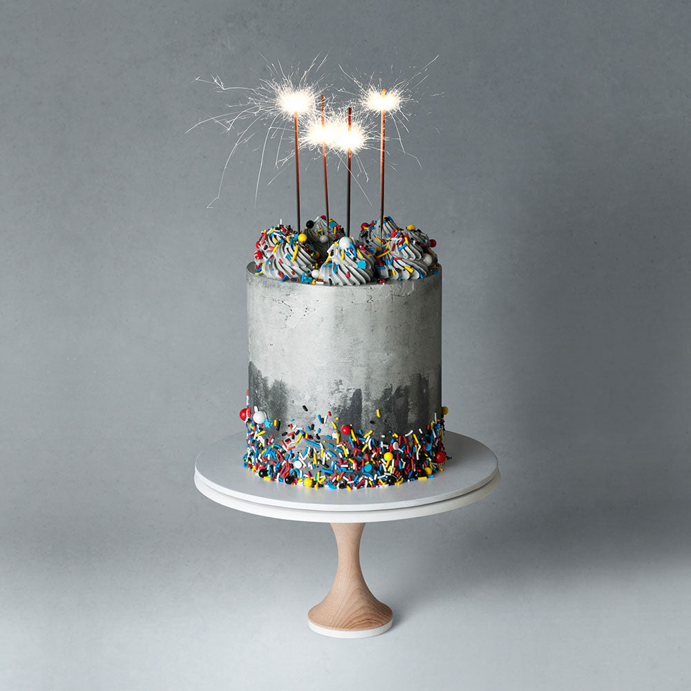 Grey buttercream cake with bright coloured sprinkles, piping, and sparklers